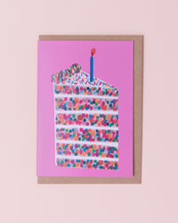 Daria Solak illustrated greetings card with brown kraft envelope. Slice of confetti birthday cake with a candle on top. Pink background
