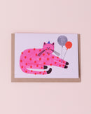 Daria Solak illustrated greetings card with brown kraft envelope. Pink cat with red dots wearing a party hat and holding balloons